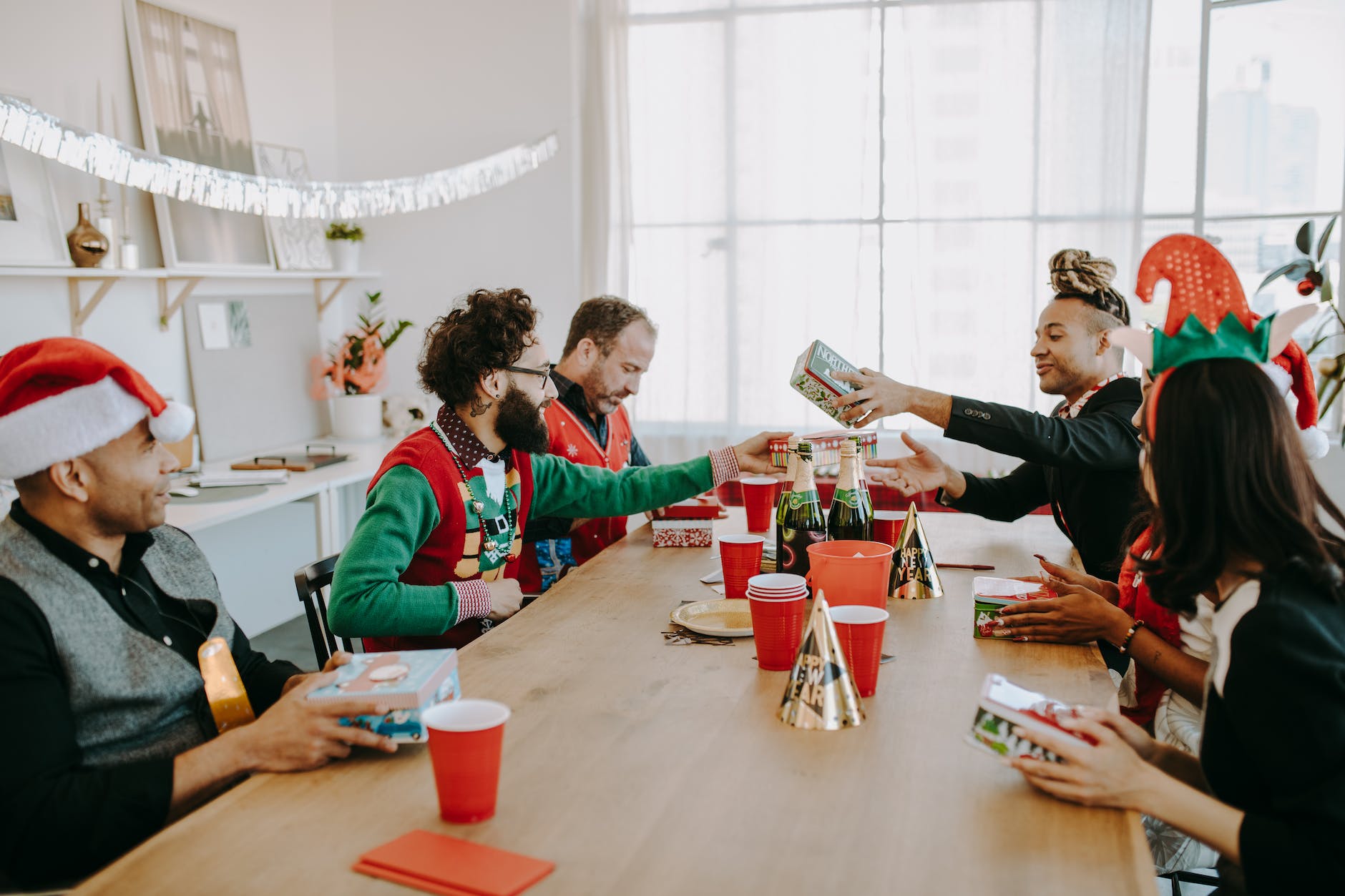 people sitting at a wooden table exchanging gifts during christmas